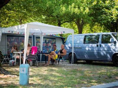 Campeggio estivo con furgone e persone sotto un gazebo.