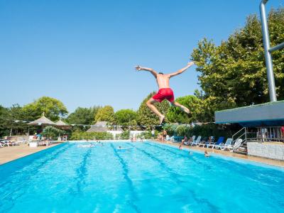 Ragazzo salta in piscina, giornata soleggiata.
