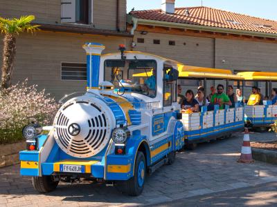 Trenino turistico colorato con passeggeri, vicino a un edificio.
