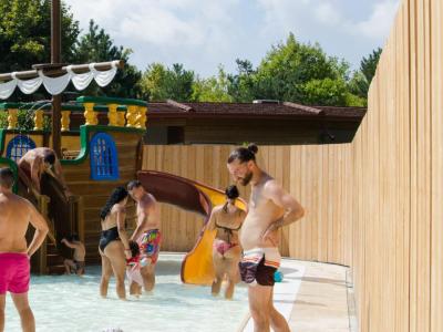 Famiglie felici giocano in piscina con scivoli e sole estivo.