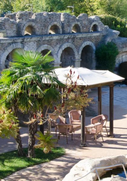 Sunny garden with stone arches, chairs, and lush nature.