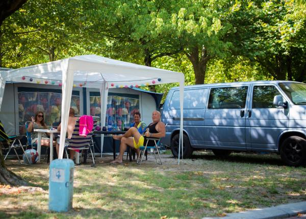 Campeggio estivo con furgone e persone sotto un gazebo.