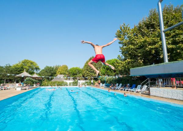 Ragazzo salta in piscina, giornata soleggiata.