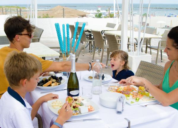 Famiglia pranza all'aperto vicino al mare, con cibo e bevande.